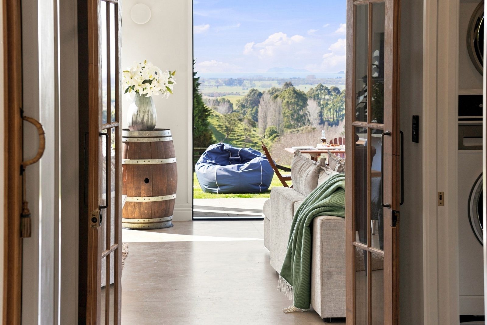 A room with a view of a landscape, a wooden barrel, a vase with flowers, and a bean bag chair.