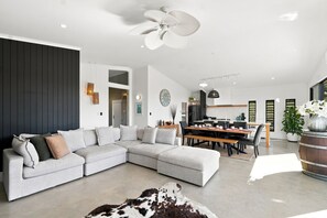 Una sala moderna con un sofá modular, un comedor y una cocina al fondo.