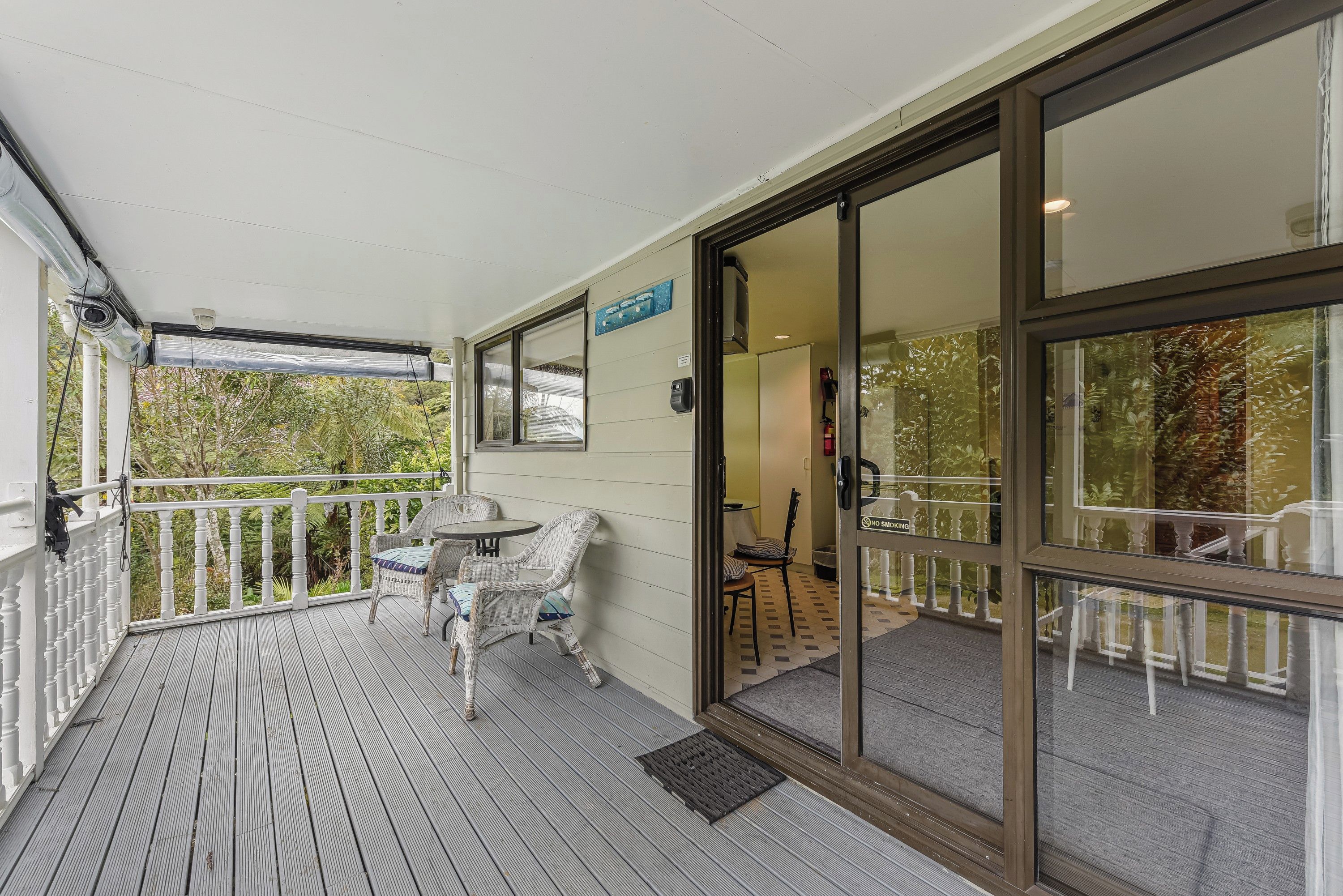 A covered outdoor area with a wooden deck, wicker furniture, and a glass door leading inside.