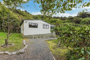 A single-story house with a sloped roof, a visible window, and a wooden fence. - Treetops & Tide Cottage - Moetapu Holiday Home (Picton)