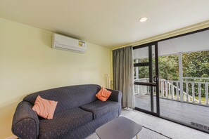 A room with a sofa, an air conditioning unit, a window with curtains, and a balcony with a railing.