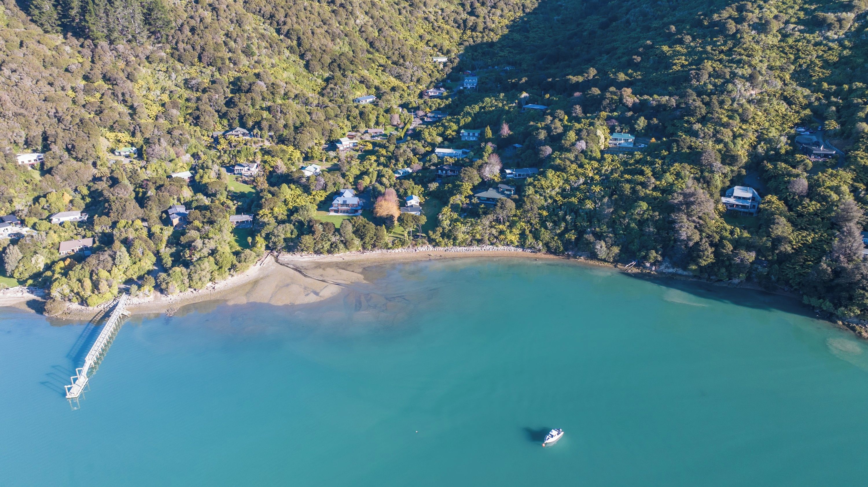 An aerial view of a coastal area with houses, a bridge, and a boat.