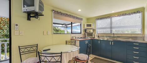 Una cocina compacta con comedor, un televisor montado en la pared y una ventana con vista a vegetación.