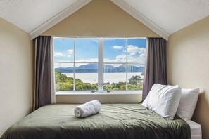 Un dormitorio con un ventanal grande, una cama con ropa de cama verde y vistas a un lago y montañas.