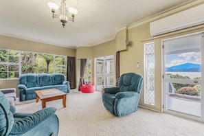 A spacious living room with a large window, a chandelier, and a view of the outdoors. - The Bay House - Moetapu Holiday Home (Picton)
