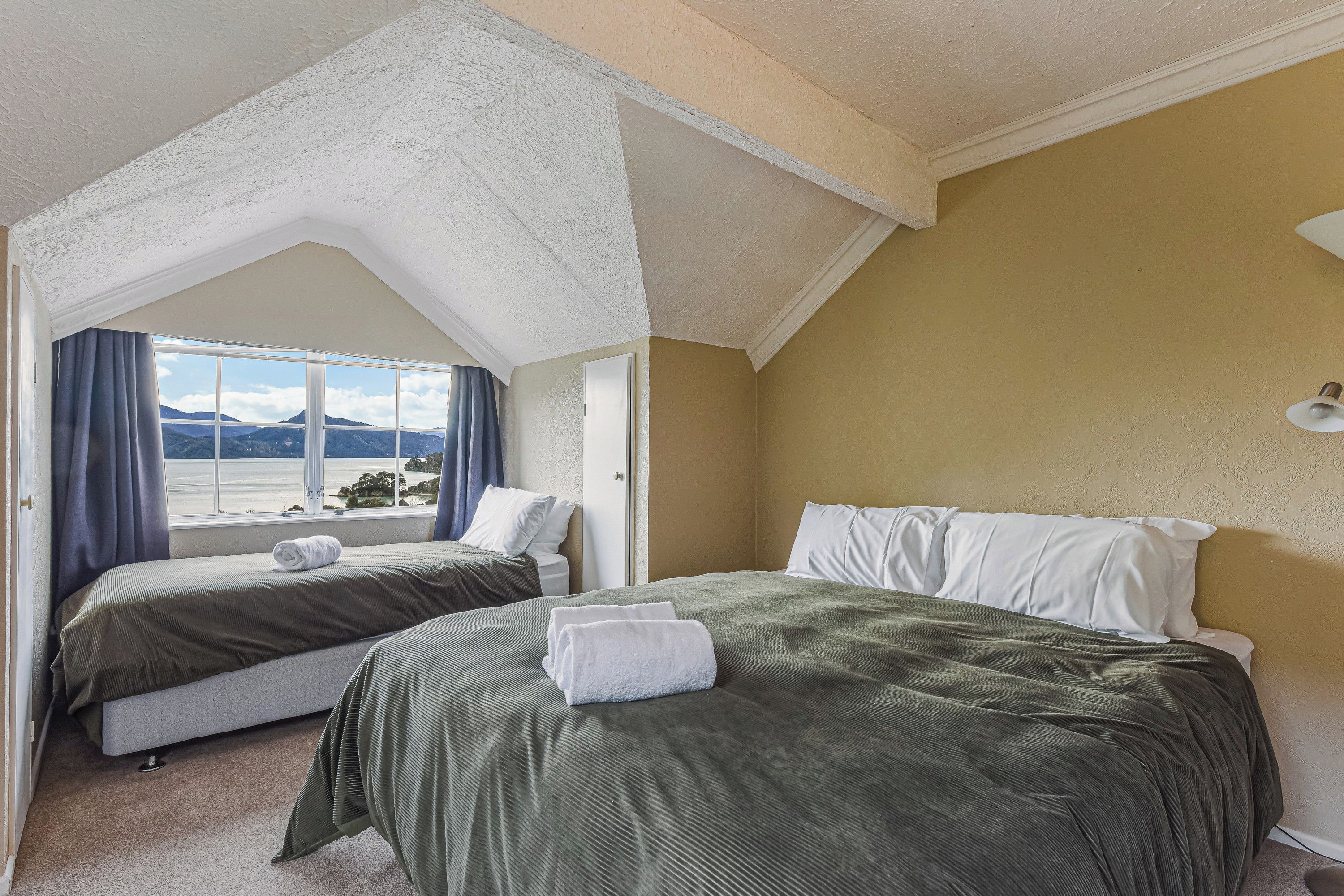 Een hotelkamer met twee bedden, een groot raam en een mooi uitzicht, en een hoge plafond.