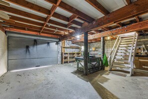An interior with a closed garage door, wooden beams, a concrete floor, and a staircase. - The Bay House - Moetapu Holiday Home (Picton)