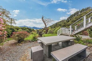 Un área de estar al aire libre con una mesa y bancos, rodeada de vegetación y vistas a montañas.