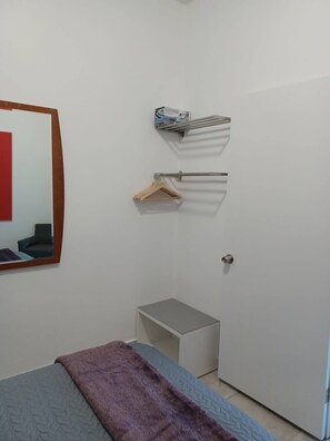 Ein Schlafzimmer mit einem Bett, einem kleinen Nachttisch, einem Spiegel, einem Handtuchhalter und einer Tür.