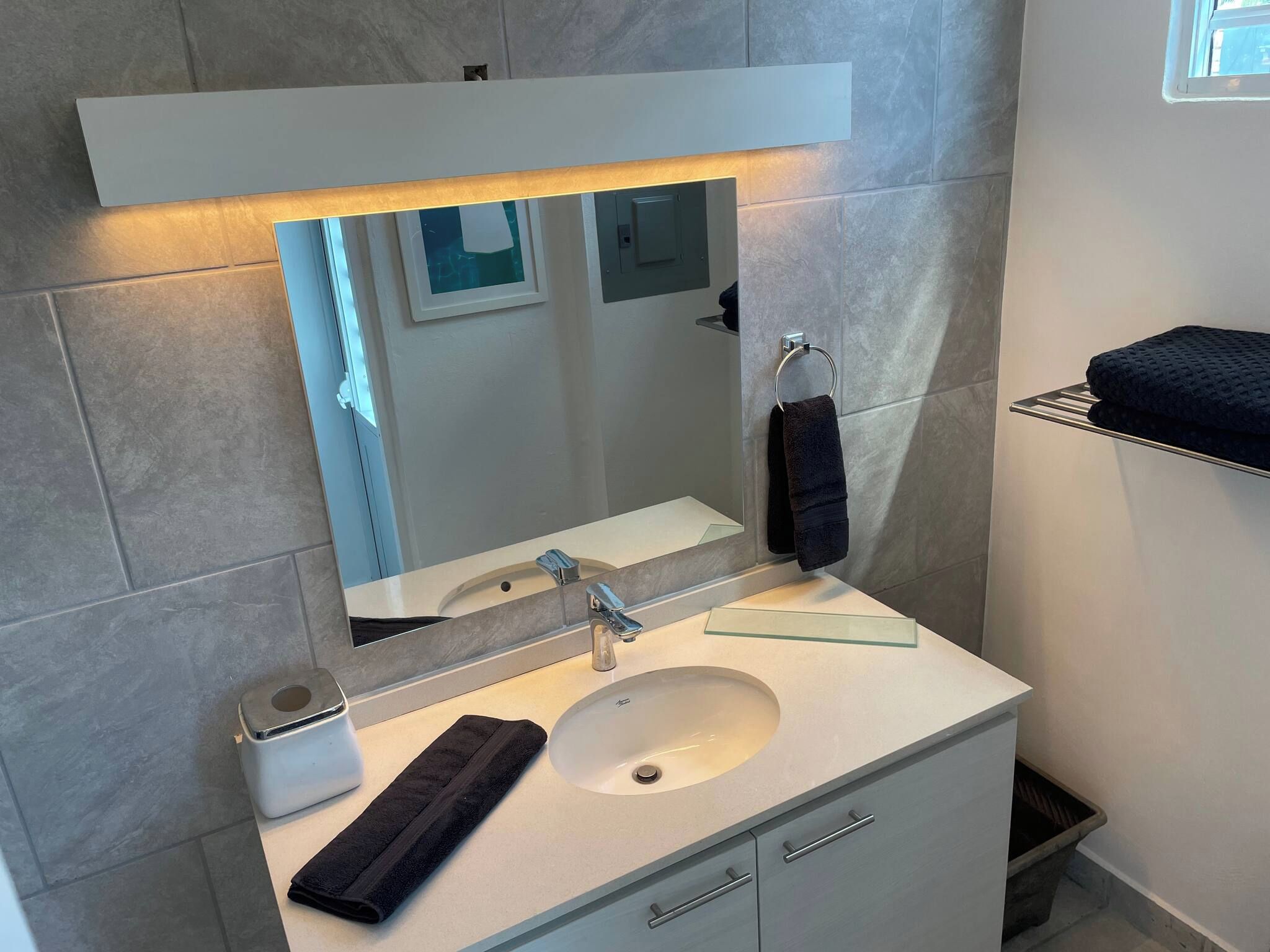 Une salle de bain moderne avec un lavabo blanc, un miroir et un porte-serviettes.