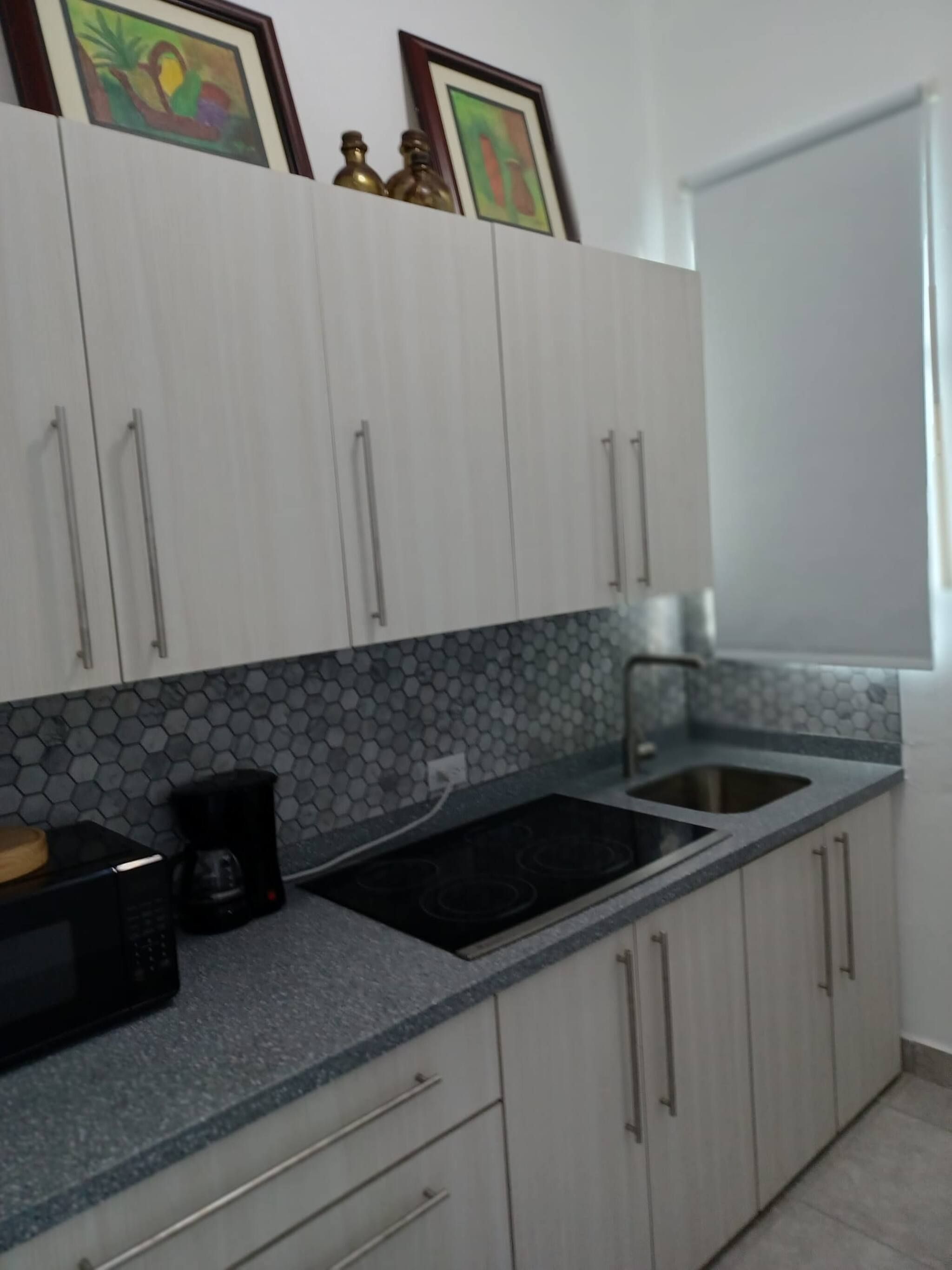 Una cocina con armarios blancos, estufa negra, un fregadero y una cafetera.