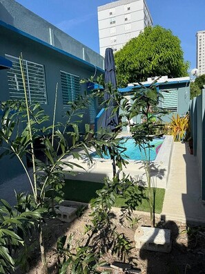 A residential area with a swimming pool, surrounded by greenery and a tall building in the background. - Lovely 2 Bedrooms Apartment With Terrace, Small Pool Share (San Juan)
