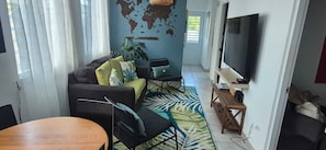 A living room with a sofa, chairs, a coffee table, a TV, and a world map on the wall. - Lovely 2 Bedrooms Apartment With Terrace, Small Pool Share (San Juan)