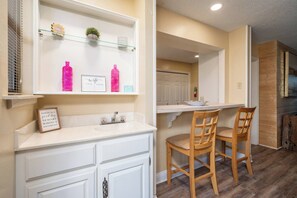 A modern kitchen with white cabinetry, a wooden dining table, and two chairs. - Emerald Isle Condo - 2bed/2bath Lots of Amenities! (Hot Springs)