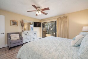 A bedroom with a bed, a dresser, a chair, a ceiling fan, a TV, and a sliding glass door to a balcony. - Emerald Isle Condo - 2bed/2bath Lots of Amenities! (Hot Springs)