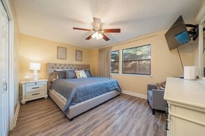 A bedroom with a bed, nightstand, bedside lamp, ceiling fan, window, and a TV mounted on the wall. - Emerald Isle Condo - 2bed/2bath Lots of Amenities! (Hot Springs)