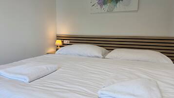 A neatly made bed with white linens and two folded towels, a bedside lamp, and a colorful abstract painting on the wall.