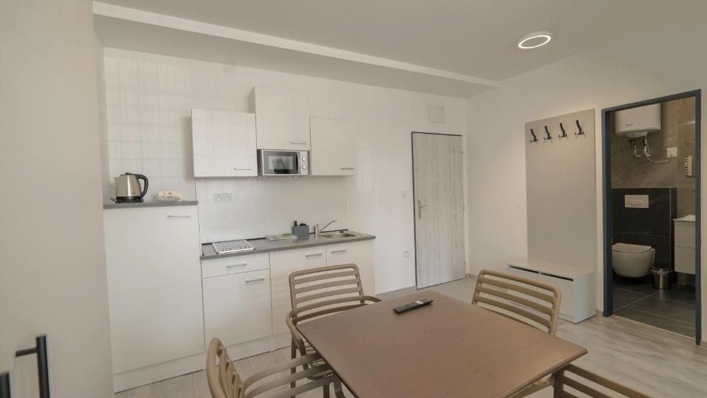 Una cucina moderna con mobili bianchi, un forno a microonde e un lavandino. C'è un tavolo da pranzo con sedie e una porta che conduce al bagno.