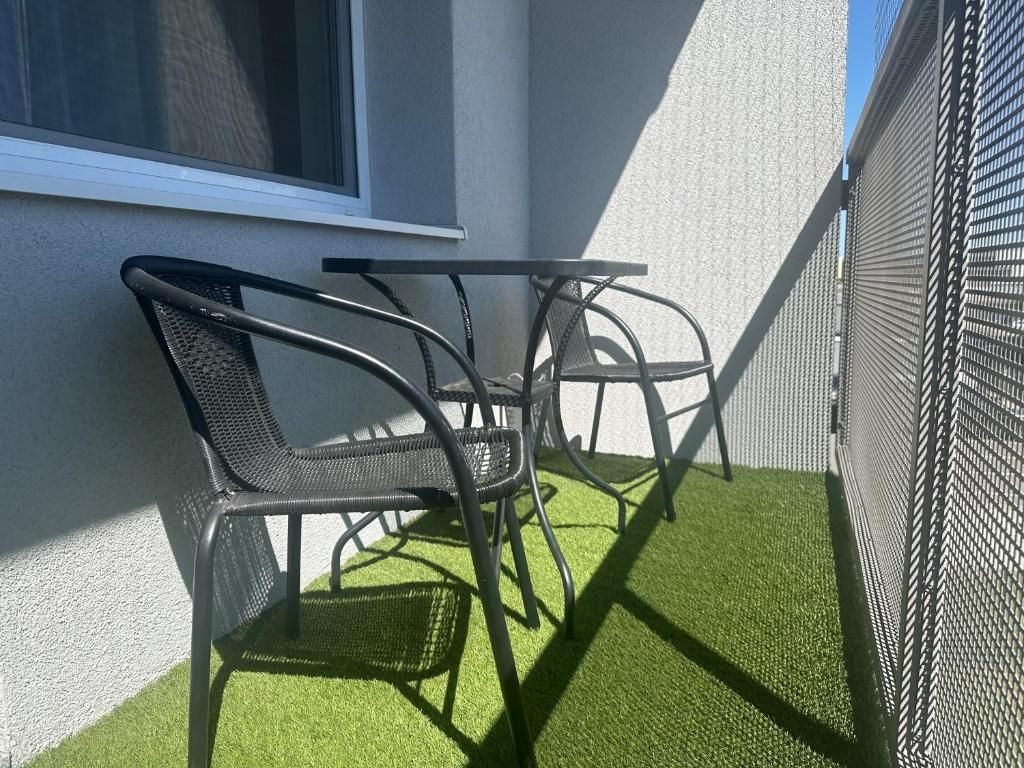 Ein kleiner Sitzbereich im Freien mit zwei Stühlen und einem Tisch, neben einem Gebäude mit einem Fenster und einer Wand.