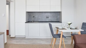 A modern kitchen with white cabinets, a grey countertop, and a dining area with a table set for two. - 111Apartments (Košický kraj)