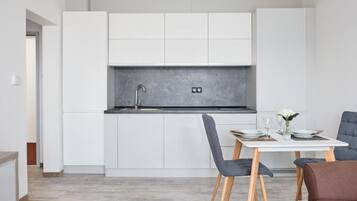 Una cocina moderna con armarios blancos, encimera gris y un comedor con una mesa dispuesta para dos personas.