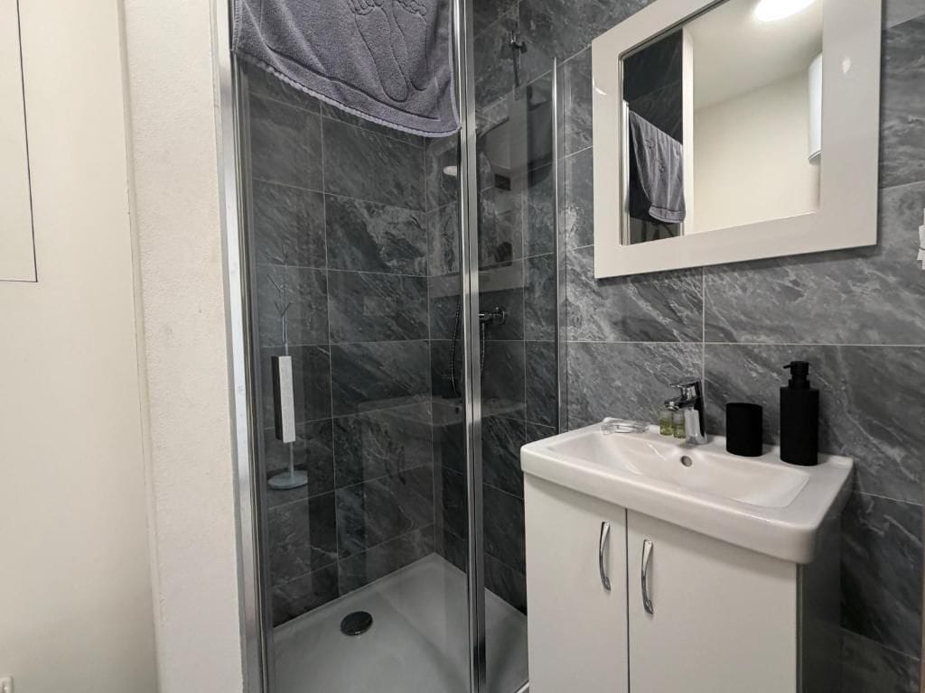 Un bany modern amb dutxa tancada amb vidre, un lavabo blanc amb un mirall a sobre i rajoles de marbre.