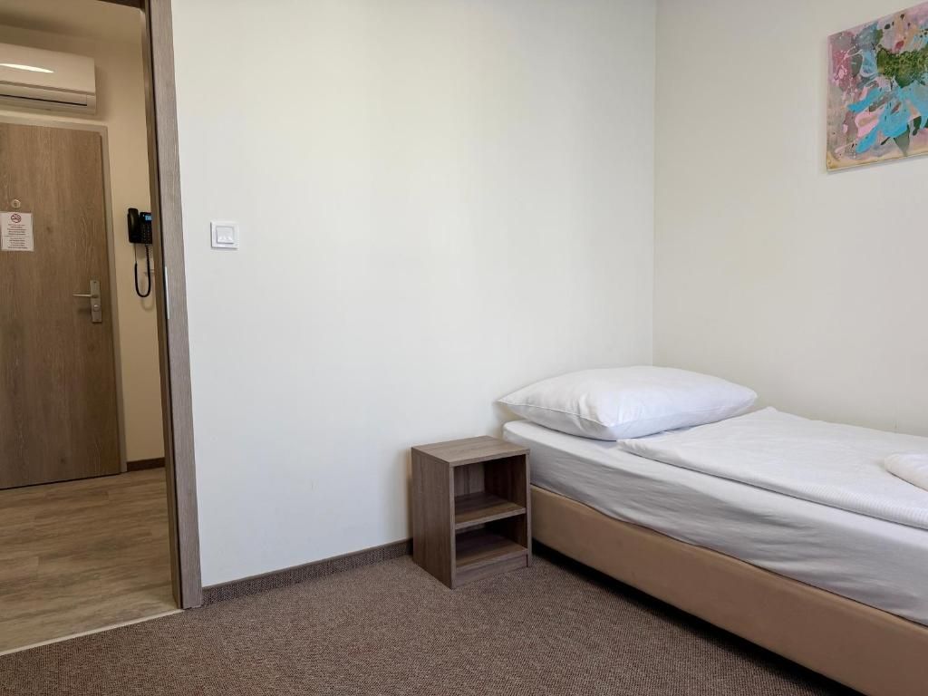 Ein Schlafzimmer mit einem Einzelbett, einem kleinen Nachttisch aus Holz und einer Tür mit Telefon.