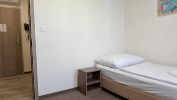 Een slaapkamer met een enkel bed, een klein houten nachtkastje en een deur met een telefoon.