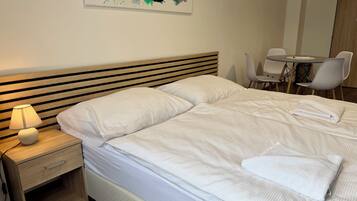 A neatly made bed with pillows, a bedside table with a lamp, and a chair at a small table.