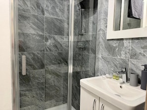 Un baño con ducha envuelta en vidrio, un lavabo blanco y un espejo sobre él.