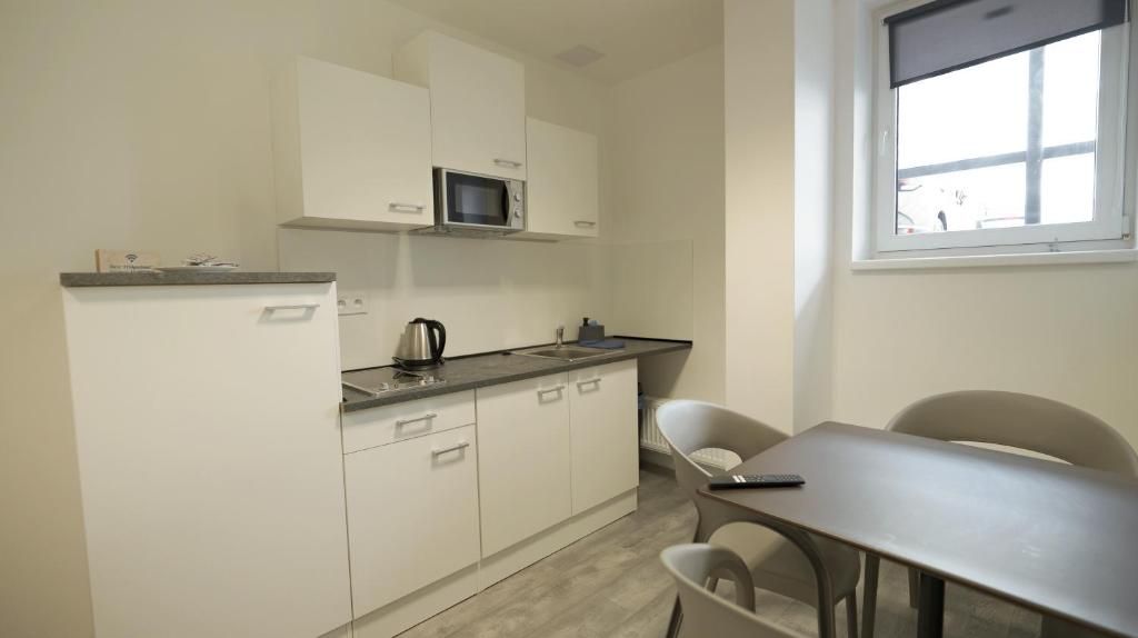 Una cocina compacta con armarios blancos, un microondas, un hervidor y una mesa de comedor con sillas.