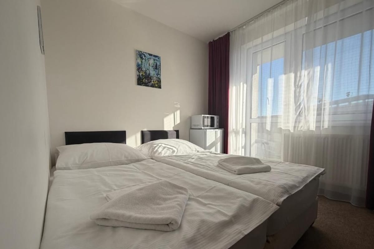 Ein Hotelzimmer mit einem Bett, einem Flachbildfernseher, einer Mikrowelle und einem Vorhangfenster.