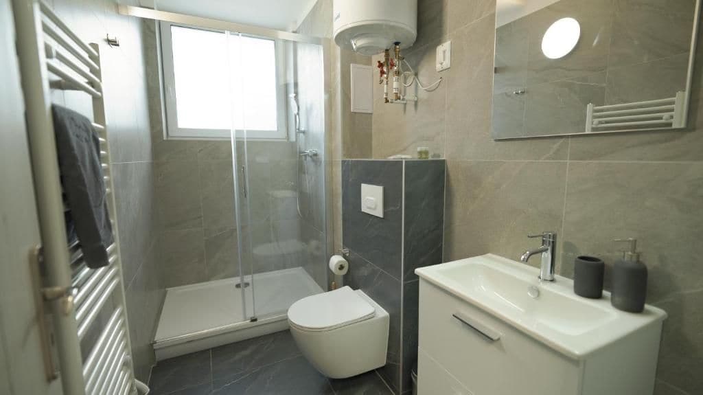 A modern bathroom with a glass shower enclosure, a toilet, a sink with a mirror, and a towel rack.