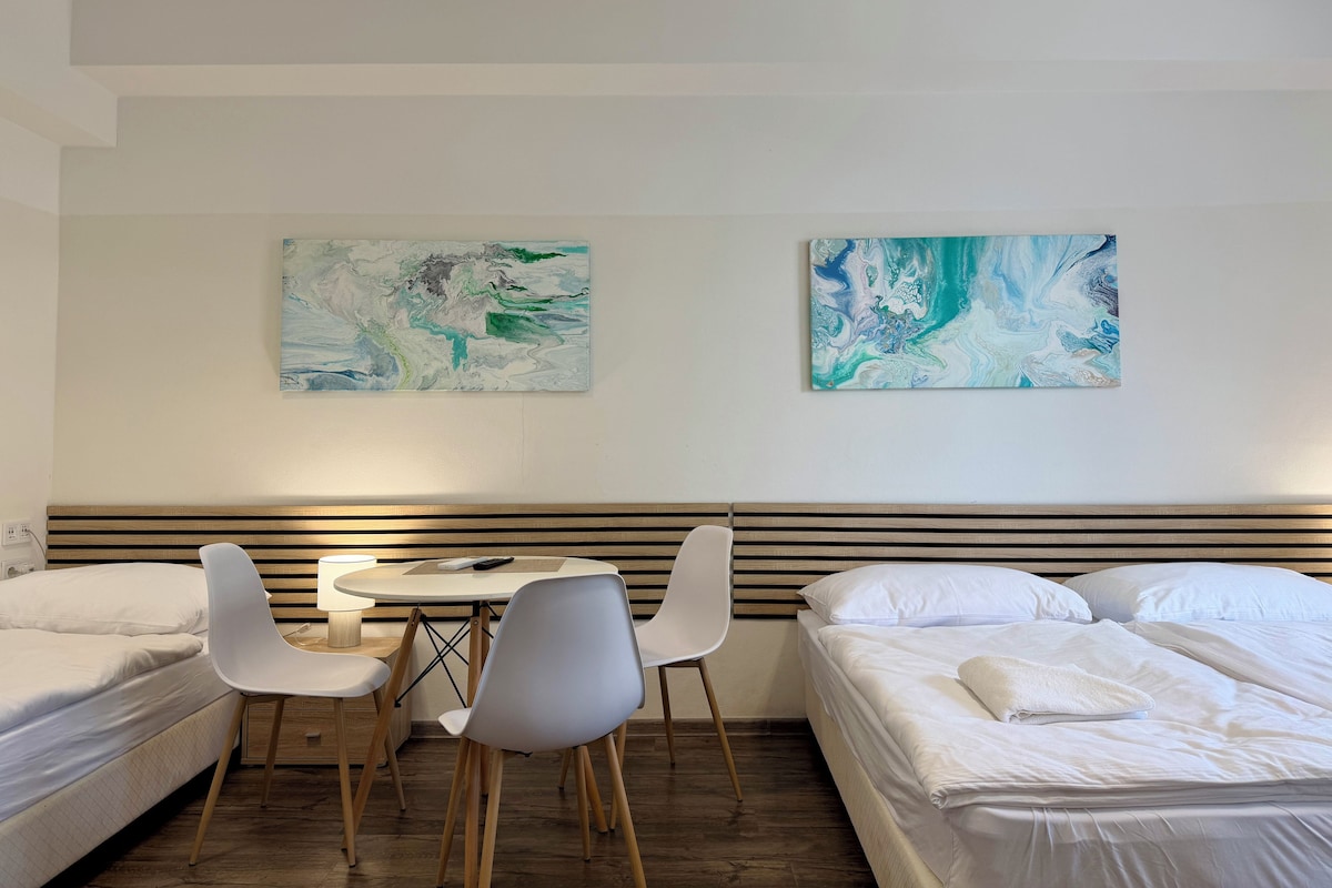 Ein Hotelzimmer mit zwei Betten, einem Esstisch und zwei Stühlen. An der Wand befinden sich abstrakte Gemälde.