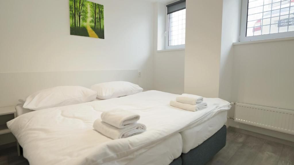 A clean, white hotel room with a bed, two pillows, a window, and a painting on the wall.