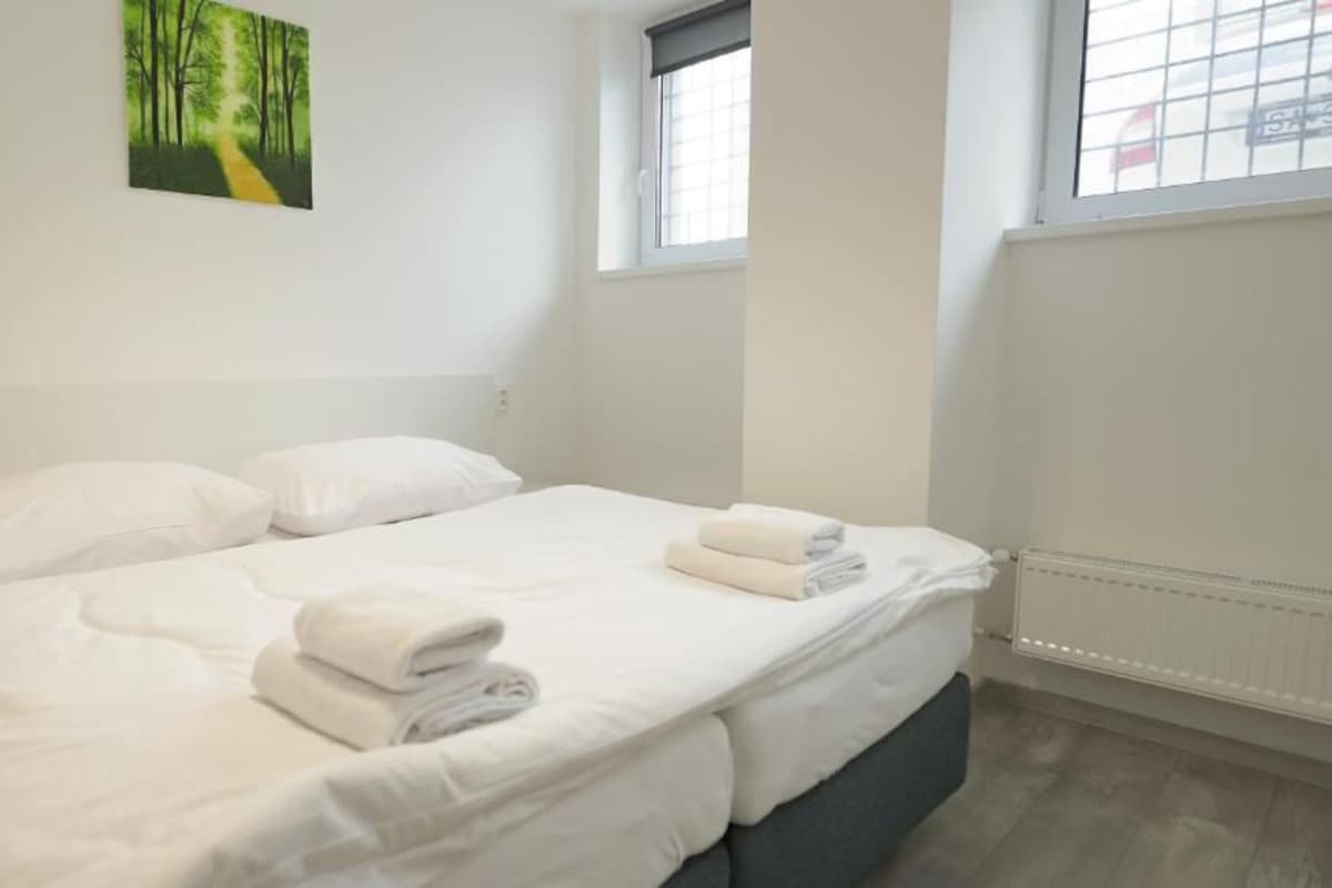 Ein sauberes, weißes Hotelzimmer mit einem Bett, zwei Kissen, einem Fenster und einem Bild an der Wand.