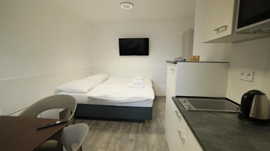 Een kleine hotelkamer met een bed, een bureau, een stoel, een televisie en een kitchenette.