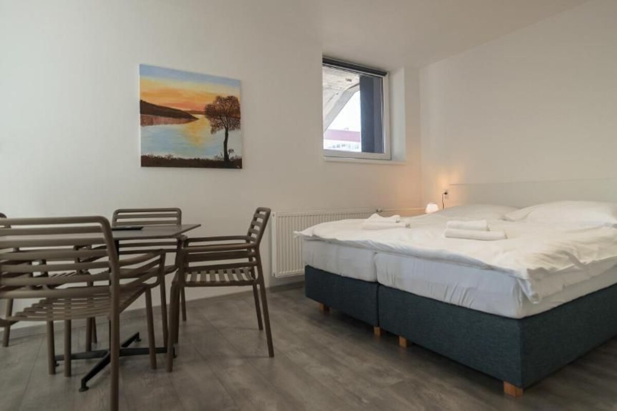 A bedroom with a bed, a desk, chairs, a window, and a painting on the wall.