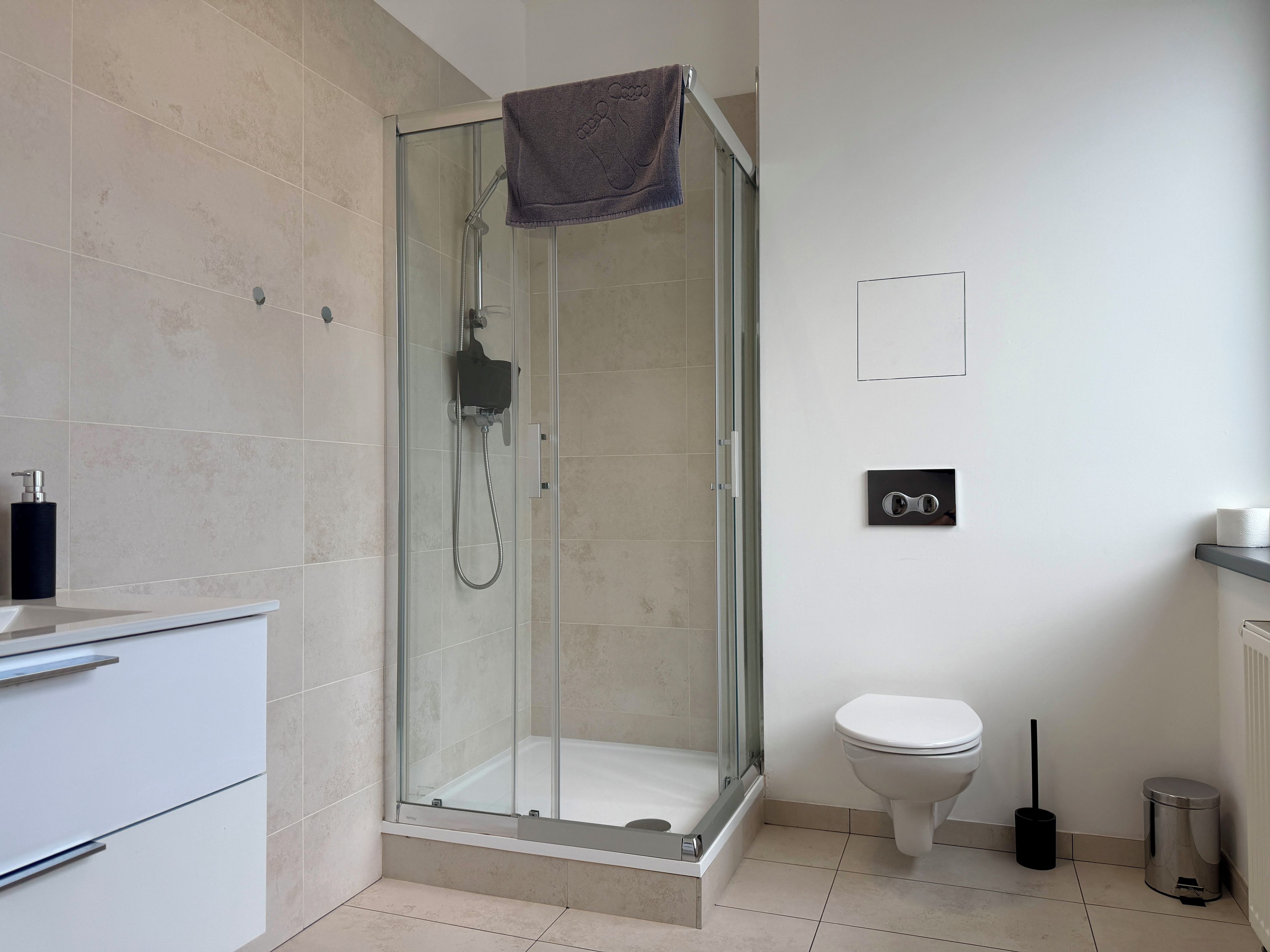 Un baño moderno con ducha envuelta en vidrio, inodoro y lavamanos con toallero.