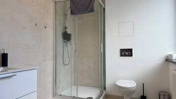 Un baño moderno con ducha envuelta en vidrio, inodoro y lavamanos con toallero.