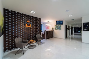 A reception area with a modern design, featuring a reception desk, two chairs, a small table with a fruit basket, and a wall with a geometric pattern.