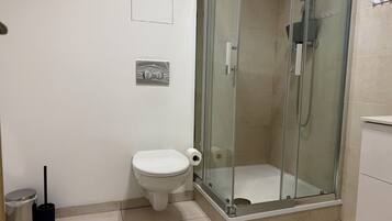 Un baño con inodoro, ducha con mampara de vidrio y un cesto de basura.