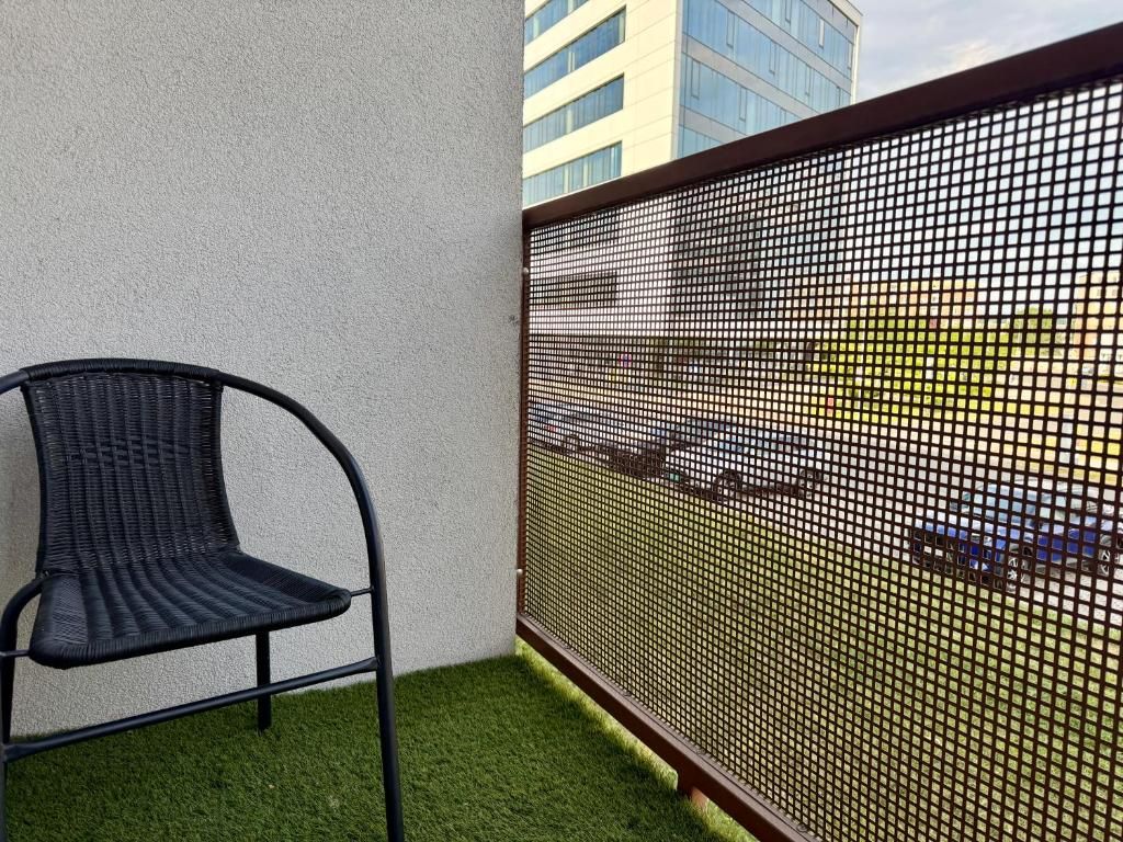 Un balcón con césped artificial, una silla de metal negro y una valla de malla metálica.