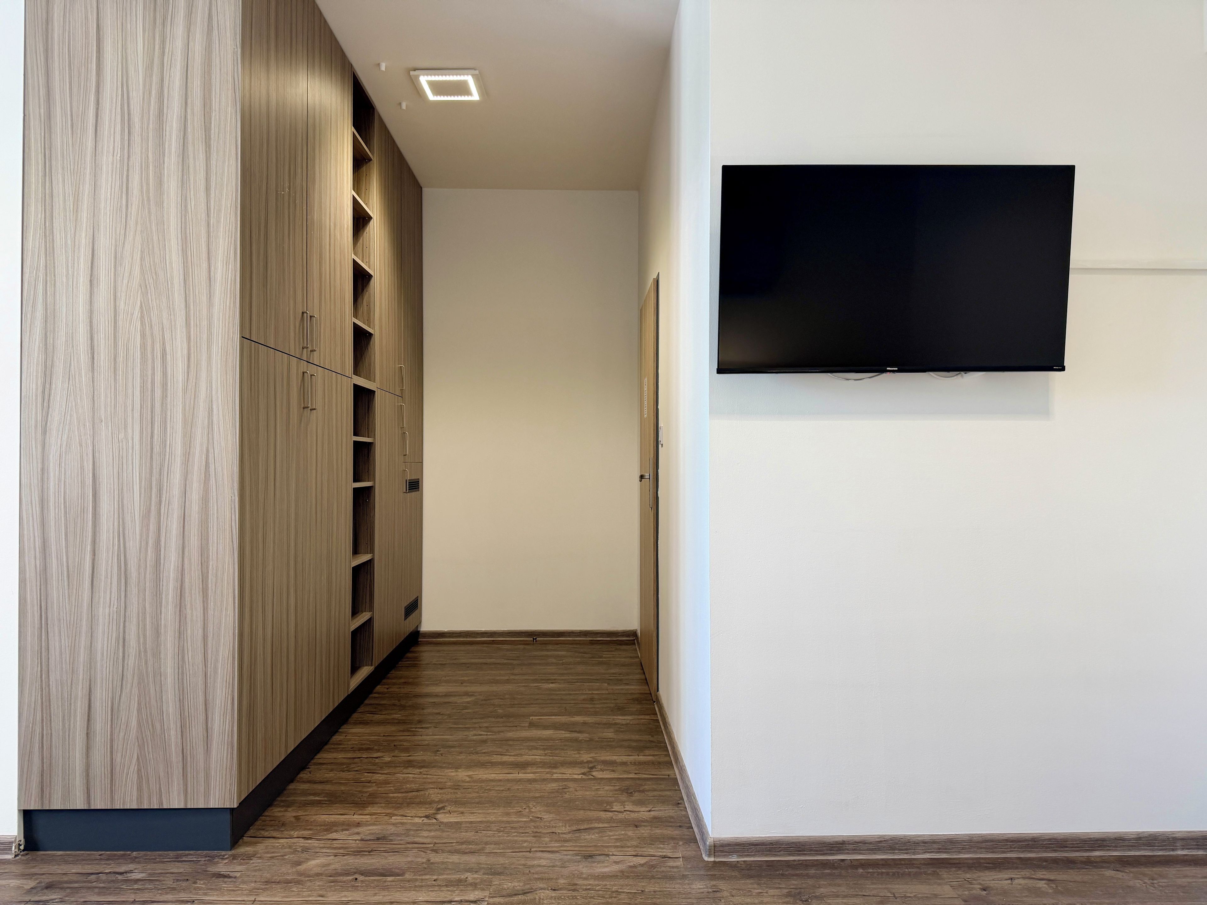 Un pasillo con suelo de madera, un armario empotrado y un televisor montado en la pared.