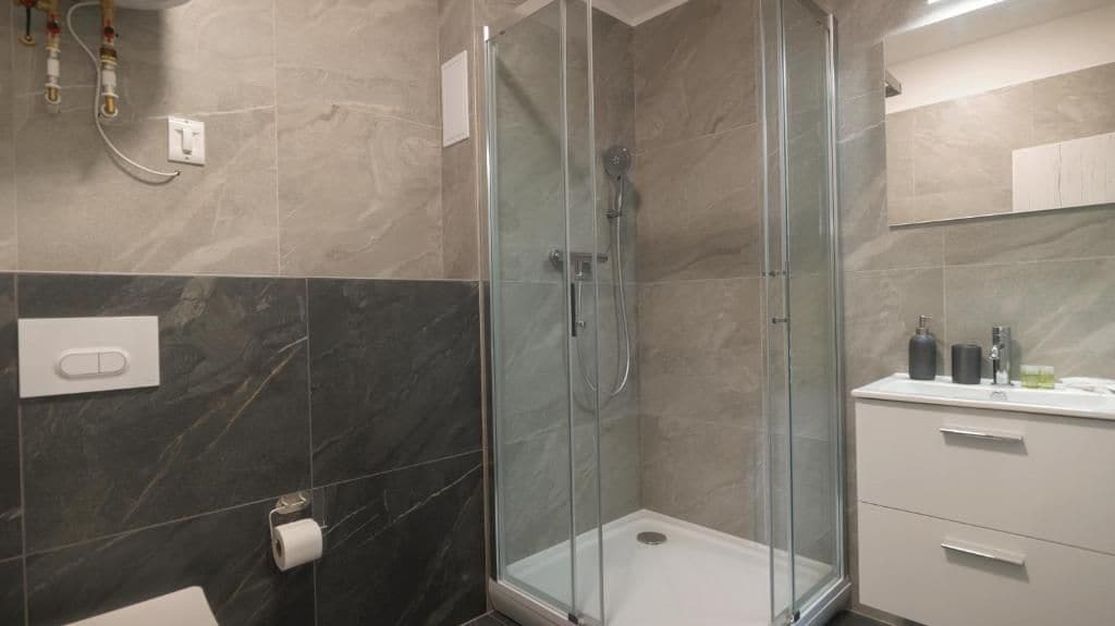 Een moderne badkamer met een douchecabine van glas, marmeren tegels, een witte wastafel en een badmeubilair met lades.