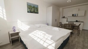 A hotel room with a bed, a desk, a chair, a small table, a microwave, and a painting on the wall.