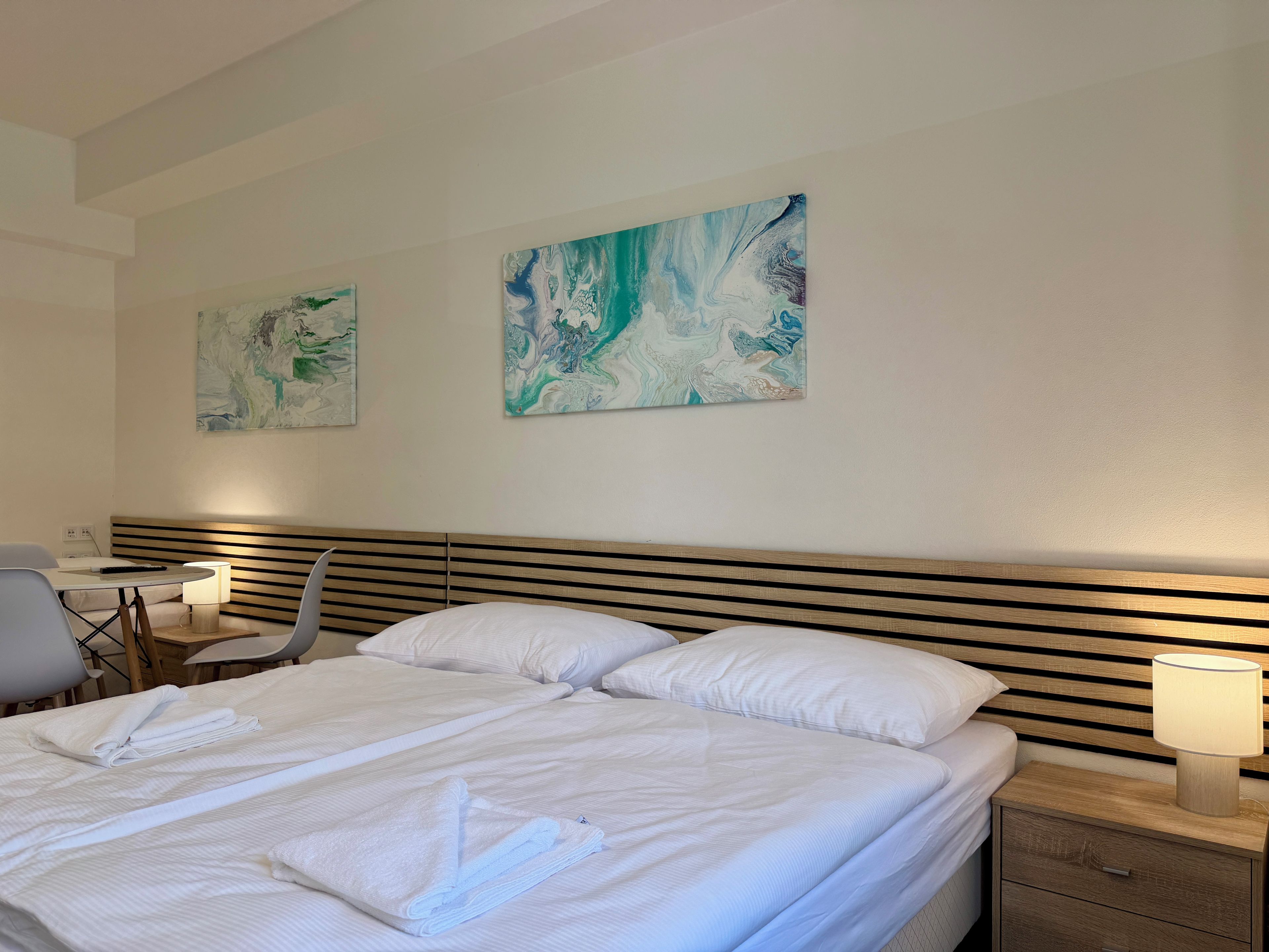 A hotel room with a bed, bedside tables, a desk with a chair, and abstract wall art.
