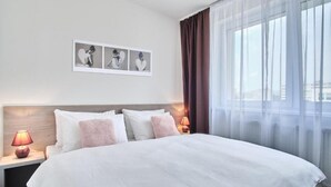 A hotel room with a large bed, a nightstand with a lamp, and a window with sheer curtains. - 111Apartments (Košický kraj)