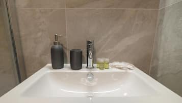 A bathroom with a white sink, a black bottle, a silver faucet, and a glass bottle.
