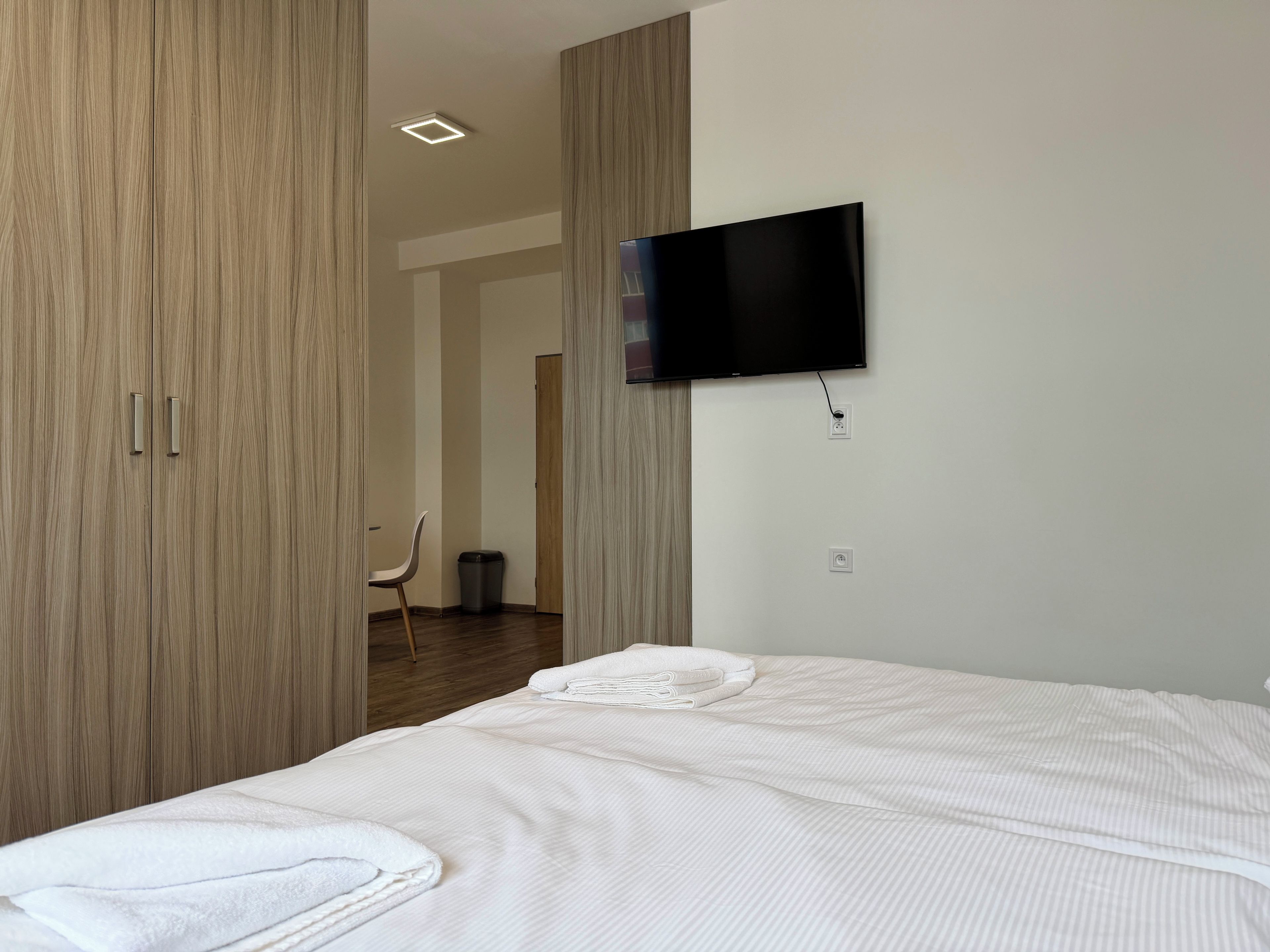 A hotel room with a bed, a TV mounted on the wall, and a wooden wardrobe.